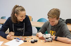 Ein Junge und ein Mädchen sitzen an einem Tisch und basteln an einem Lego-Roboter