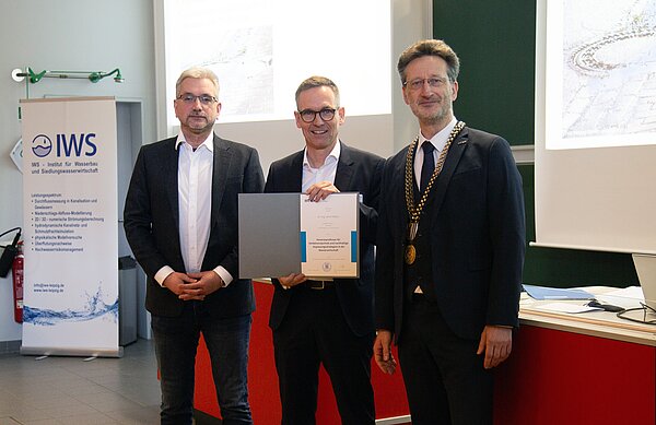 Honorarprofessor Dr. Ulrich Meyer berufen drei Männer in Anzügen stehen zusammen, der Mittlere hät eine Urkunde hoch