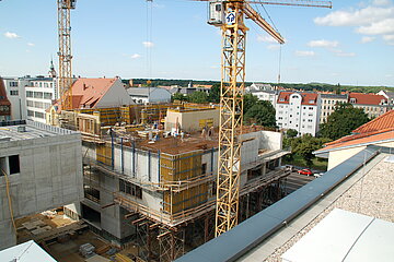 Baustelle Auf dem Bild ist ein Wohnhaus im frühen Baustadium zu sehen. Im Bildvordergrund und -hintergrund befinden sich Kräne.