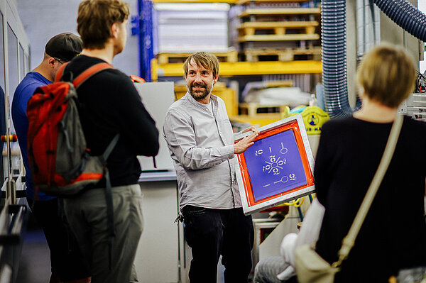 Ein Mann zeigt einer Gruppe ein Bild in einem Rahmen