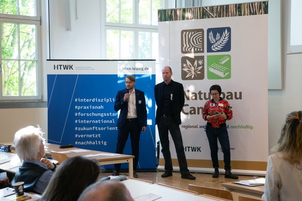 Nachhaltig Bauen und Sanieren 2026 3 Personen stehen vor großen Roll-ups und sprechen in ein Mikrofon