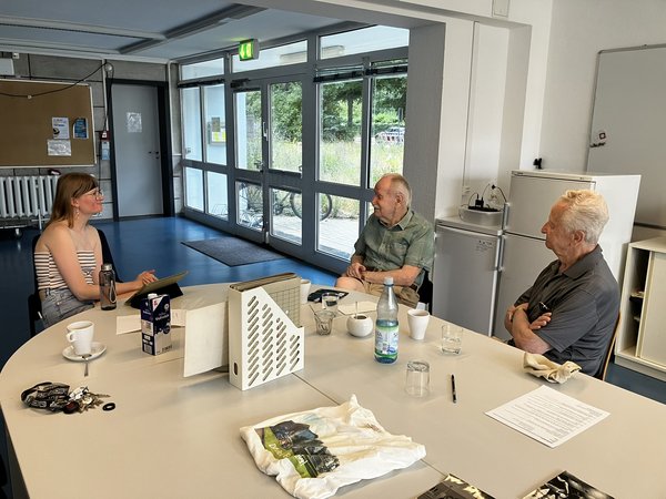 junge Frau im Gespräch mit zwei älteren Herren an einem Tisch.