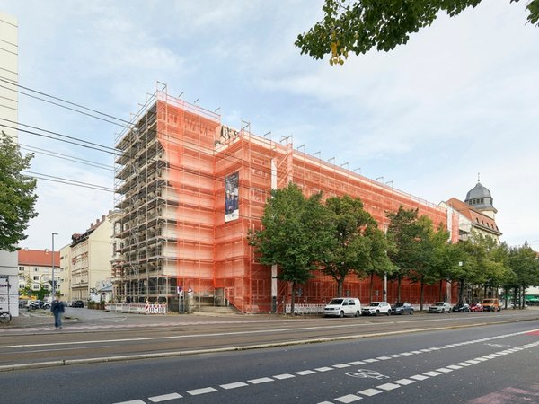 Fassadengerüst am Geutebrück-Bau der HTWK Leipzig. (Foto: Michael Moser/SIB) Eingerüstetes Gebäude mit orangen Planen an großer Straße