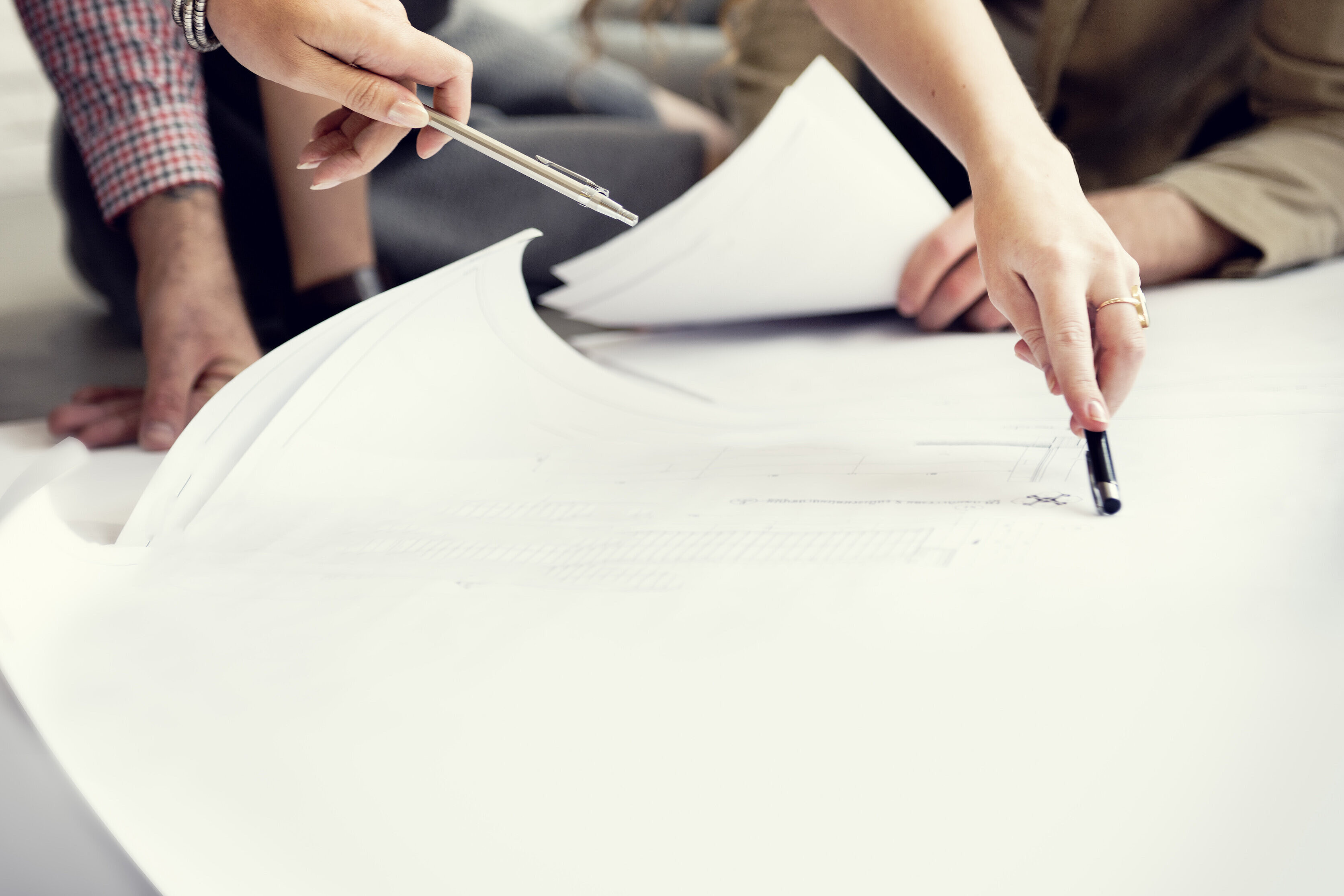 Es ist ein großes Blatt Papier zu sehen. Die Hände von zwei Personen, welche mit einem Stift auf die Skizze zeigen, sind zu sehen.