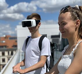 Ein Junge mit VR-Brille und ein Mädchen (jugendlich) auf einem Dach.