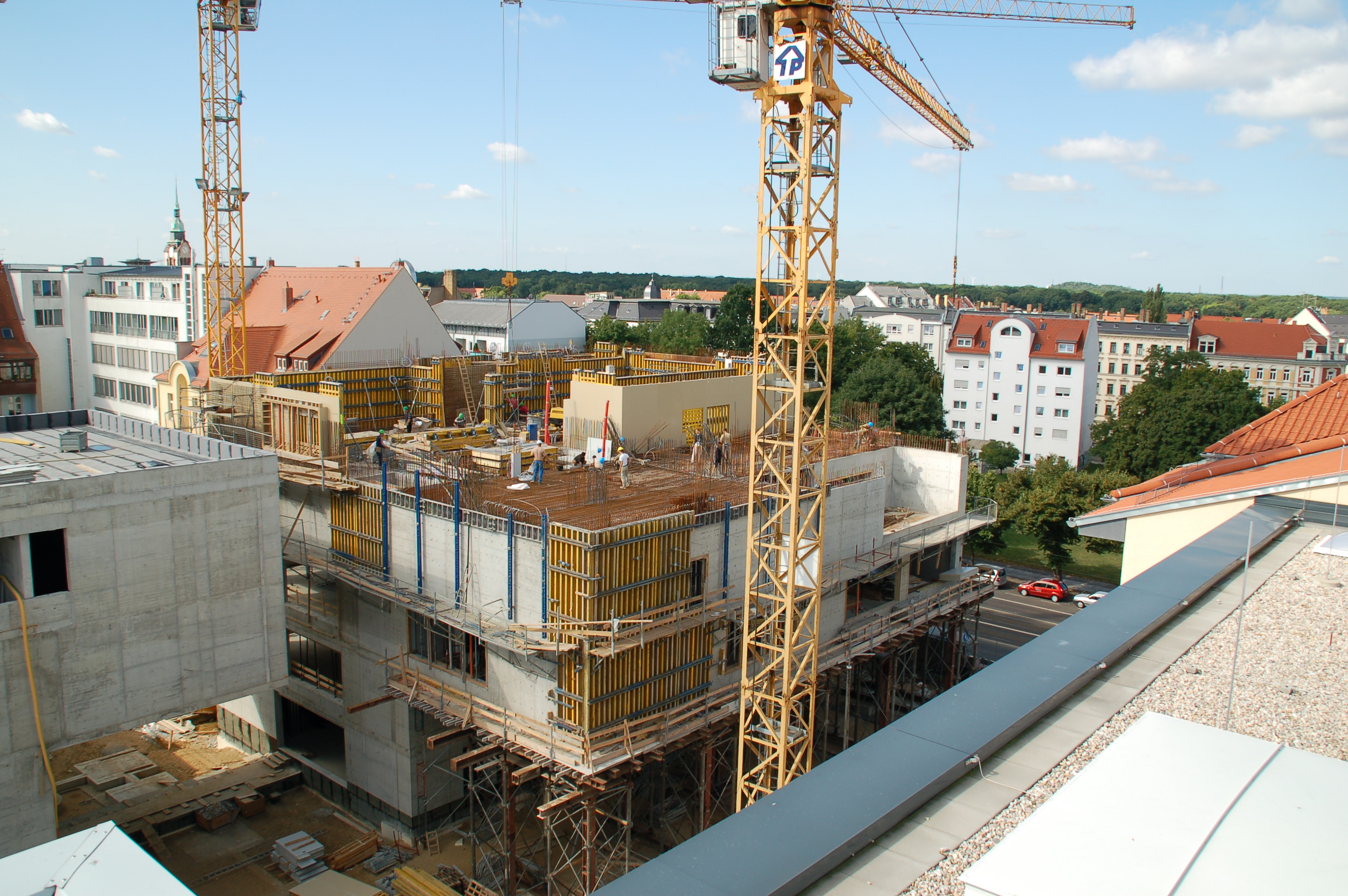 Auf dem Bild ist ein Wohnhaus im frühen Baustadium zu sehen. Im Bildvordergrund und -hintergrund befinden sich Kräne.